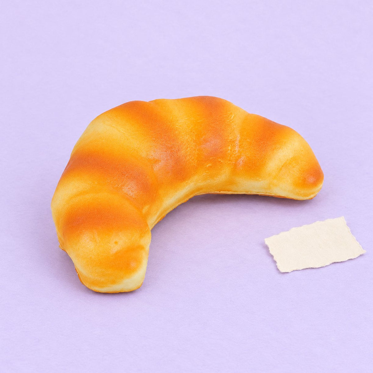 Squishy croissant slow rising 12,5 cm, realistické pečivo na pastelovém papíře
