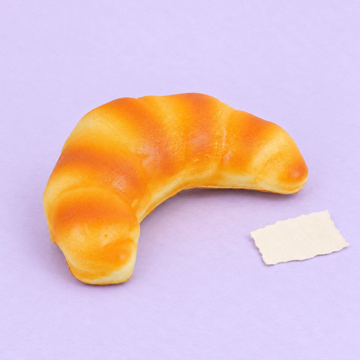 Squishy de cruasán slow rising, pan realista de 12,5 cm, sobre papel pastel