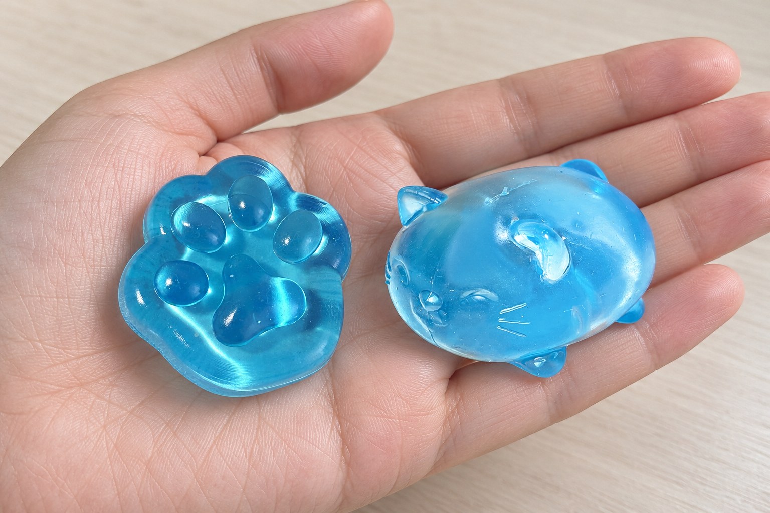 Mano abierta con un diminuto squishy de pata de gato de gelatina azul y un squishy de gato de gelatina transparente