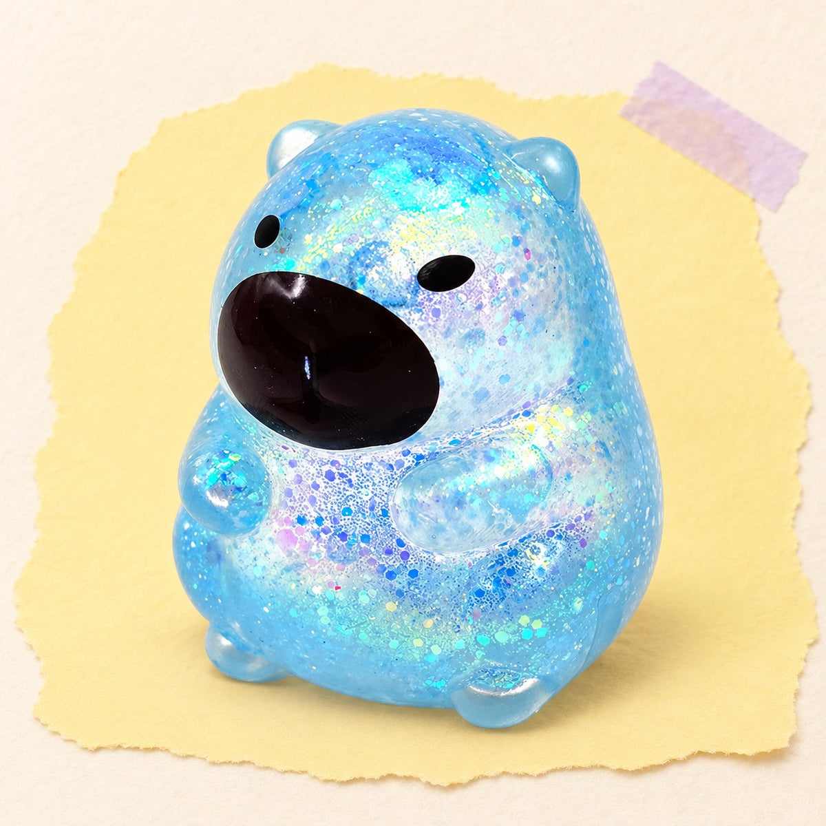 Třpytivá squishy kapybara v modré barvě se sugar náplní na pastelovém papíře
