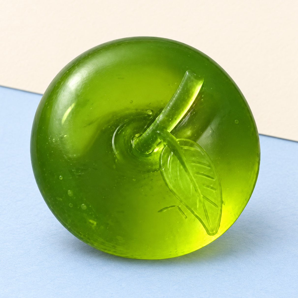 Squishy de manzana de maltosa en verde transparente, sobre papel pastel