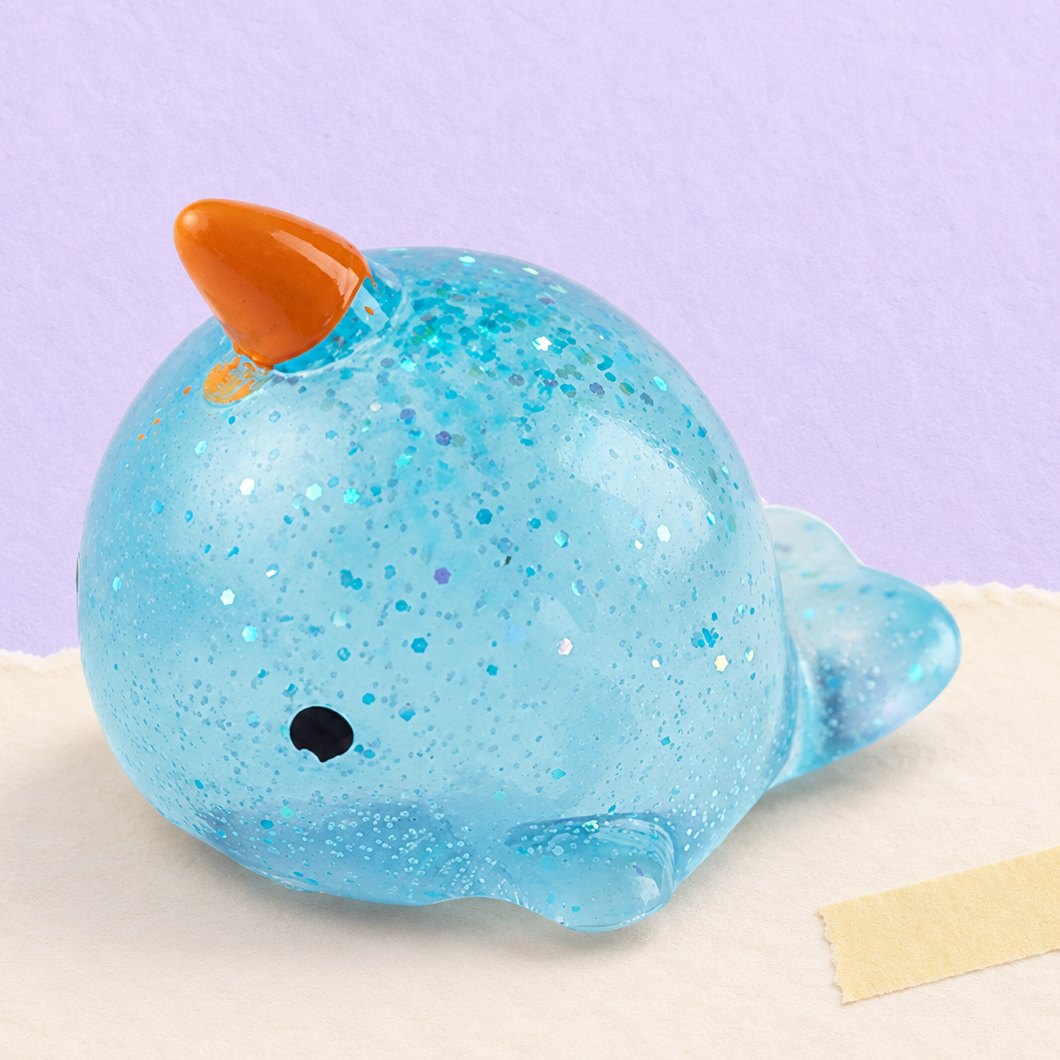 Squishy narval mochi com brilhantes, sobre papel pastel