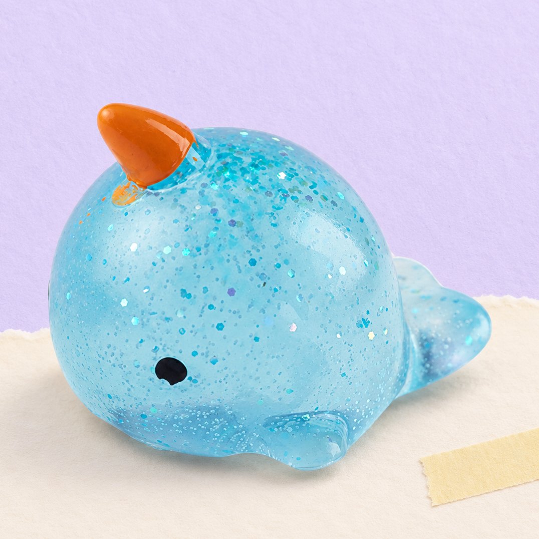 Squishy narval mochi à paillettes photographié sur papier pastel