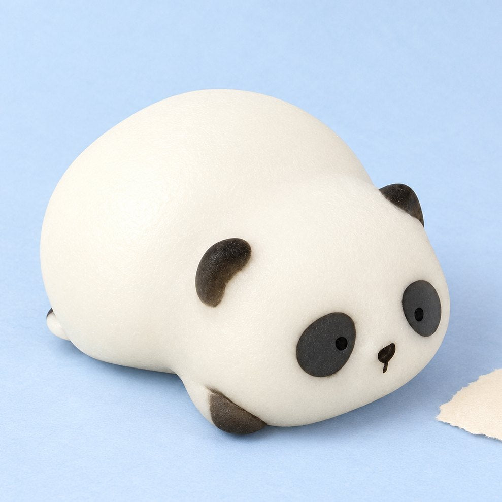 Squishy panda tumbado en su caja de regalo, sobre papel pastel