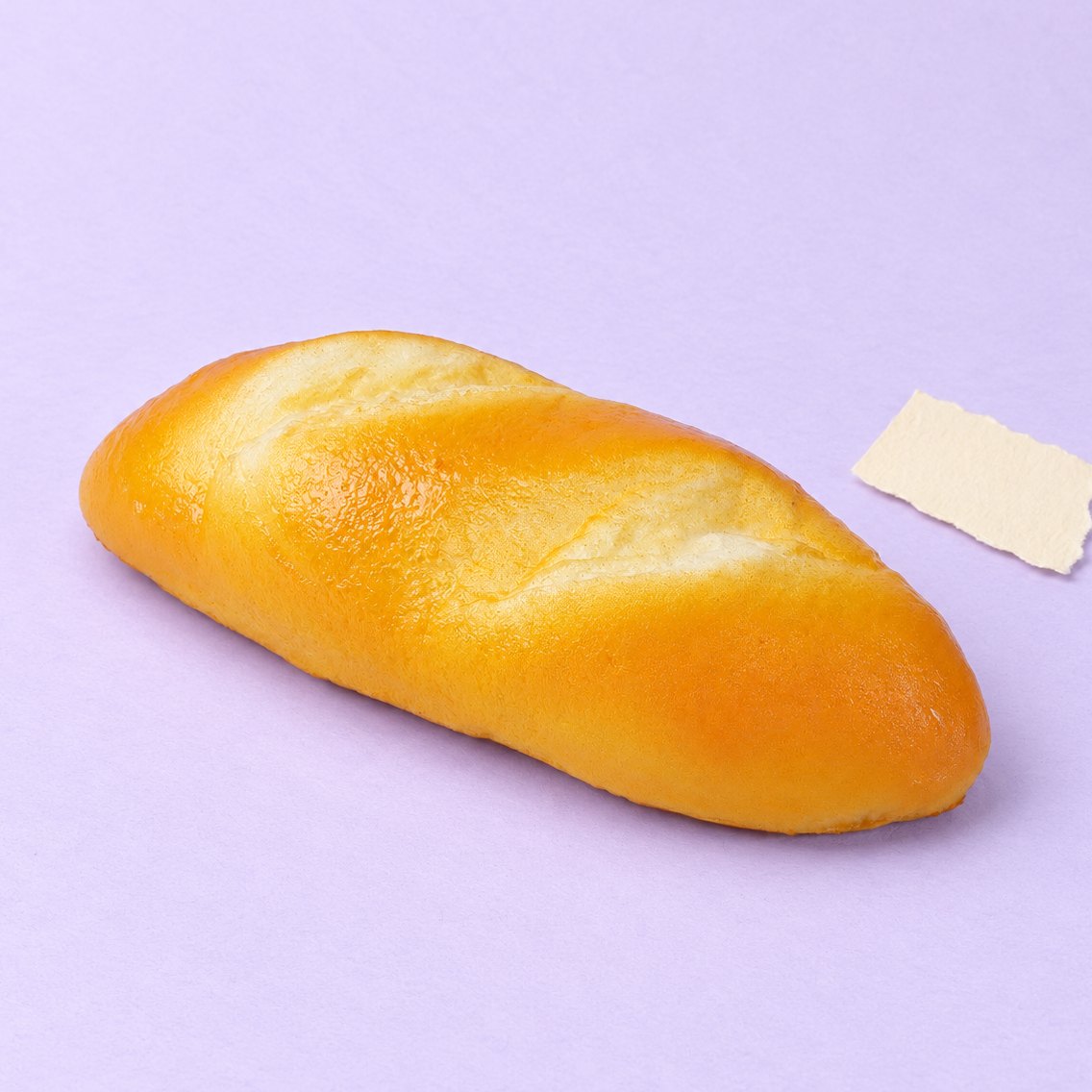Squishy pão comprido de 18 cm, tipo pão de leite, sobre papel pastel