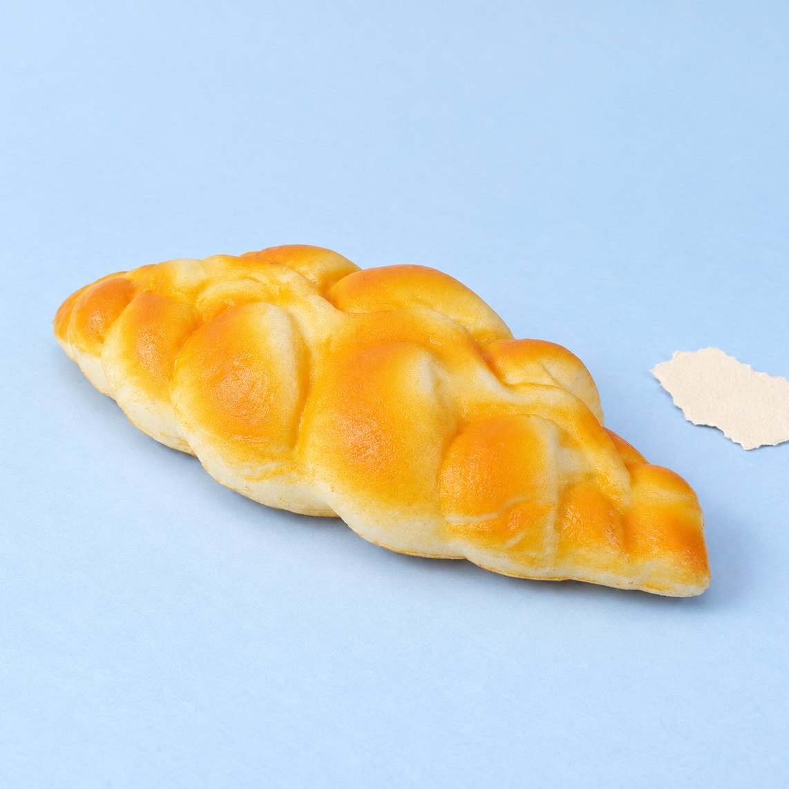 Squishy pão entrançado slow rising de 19 cm, sobre papel cor pastel