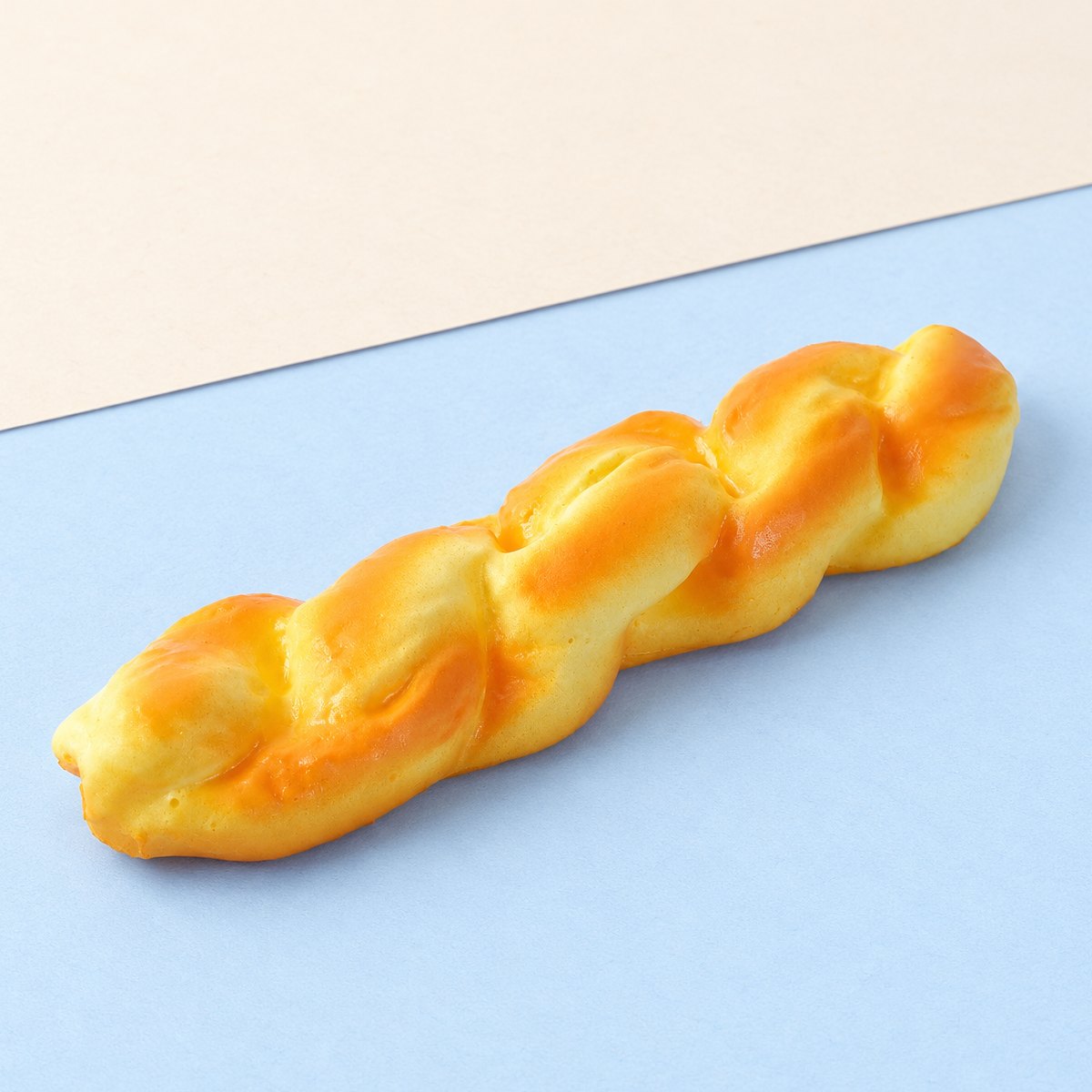 Squishy pão torcido slow rising, comprido, com 20 cm, sobre papel cor pastel