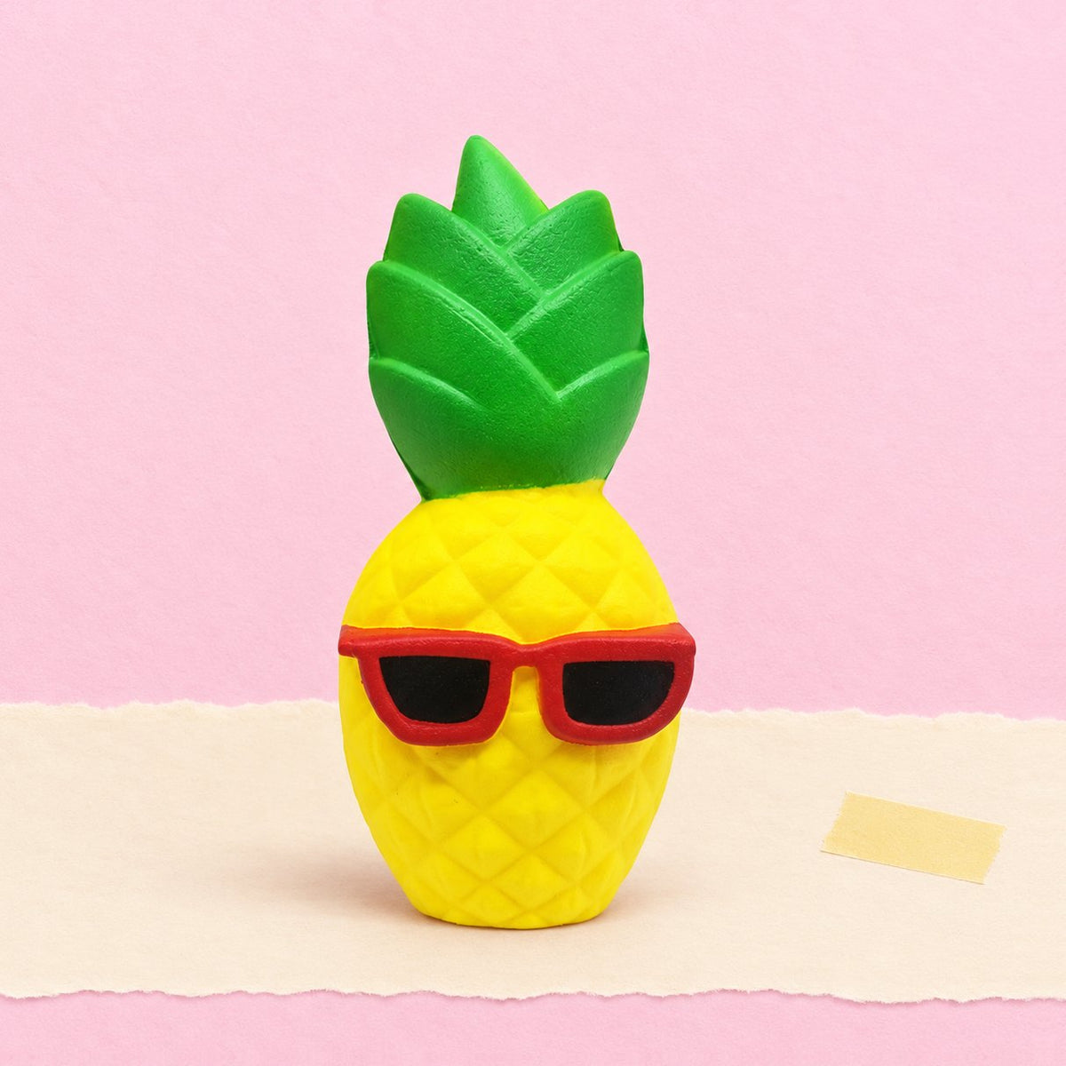 Squishy gigante de piña con gafas de sol, sobre papel pastel