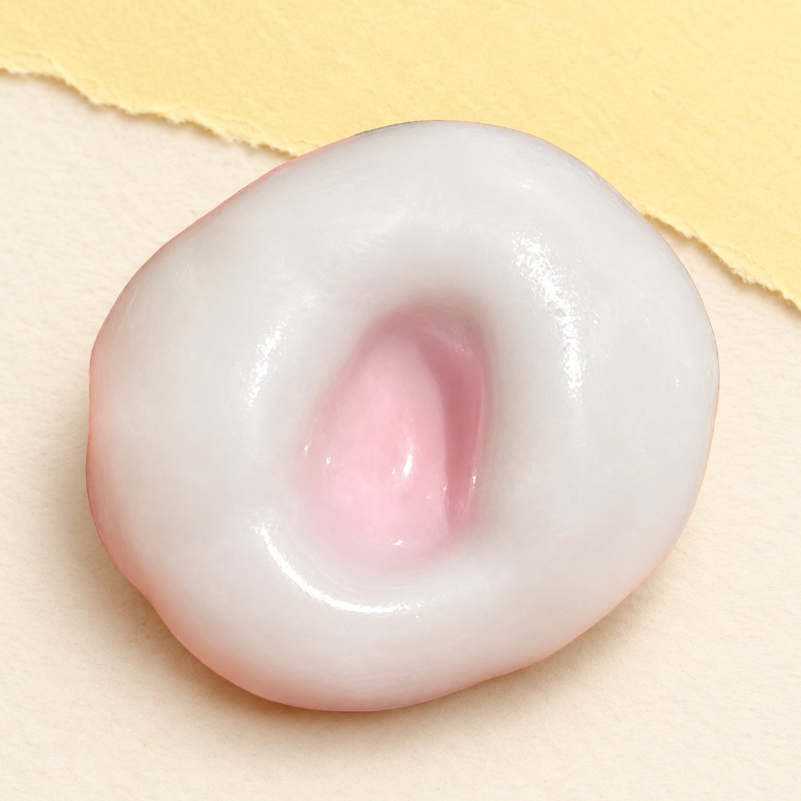 Squishy rýžový koláček v jahodově růžové barvě s pružnou slupkou na pastelovém papíře