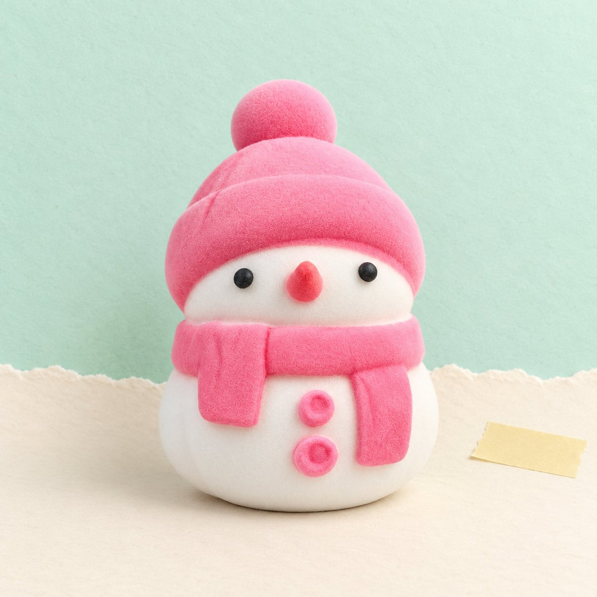 Squishy sněhulák měkký jako mochi, růžový v sáčku, na pastelovém papíře