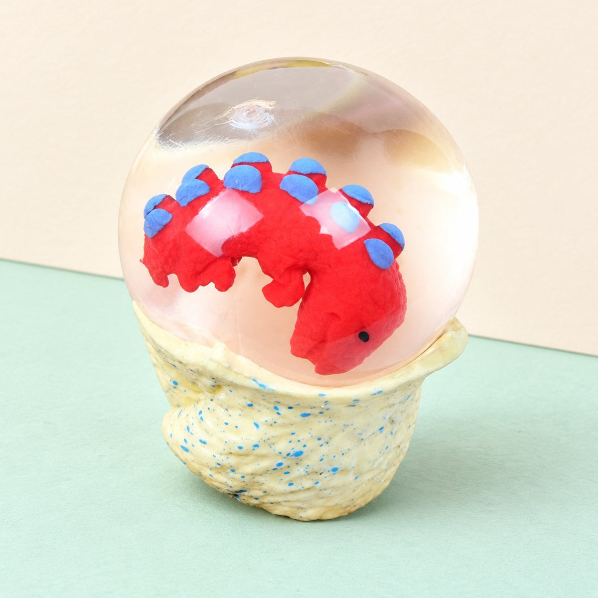 Squishy uovo di dinosauro con baby dino dentro, su carta pastello