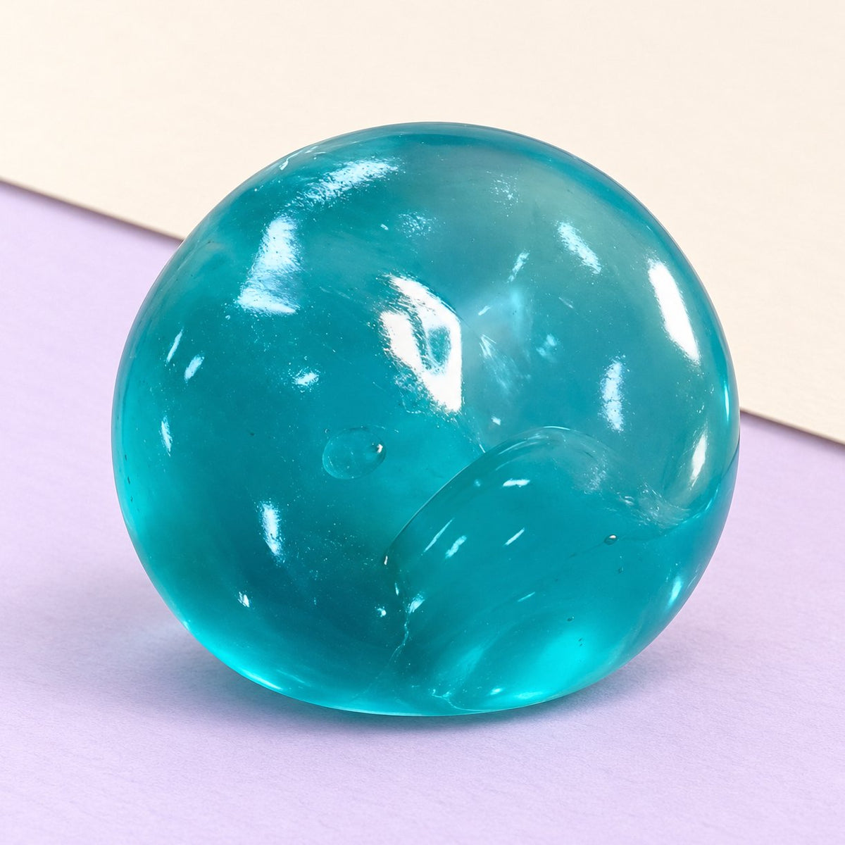 Squishy z maltózy, pomalu se zvedající gelová kulička v oceánově modré barvě na pastelovém papíře
