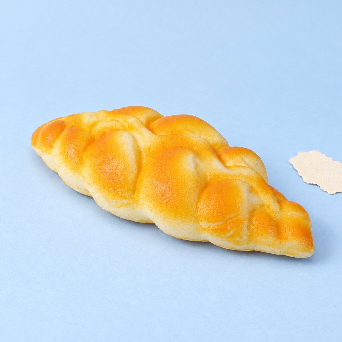 Vlechtbrood squishy van 19 cm, gevlochten brood op pastelkleurig papier